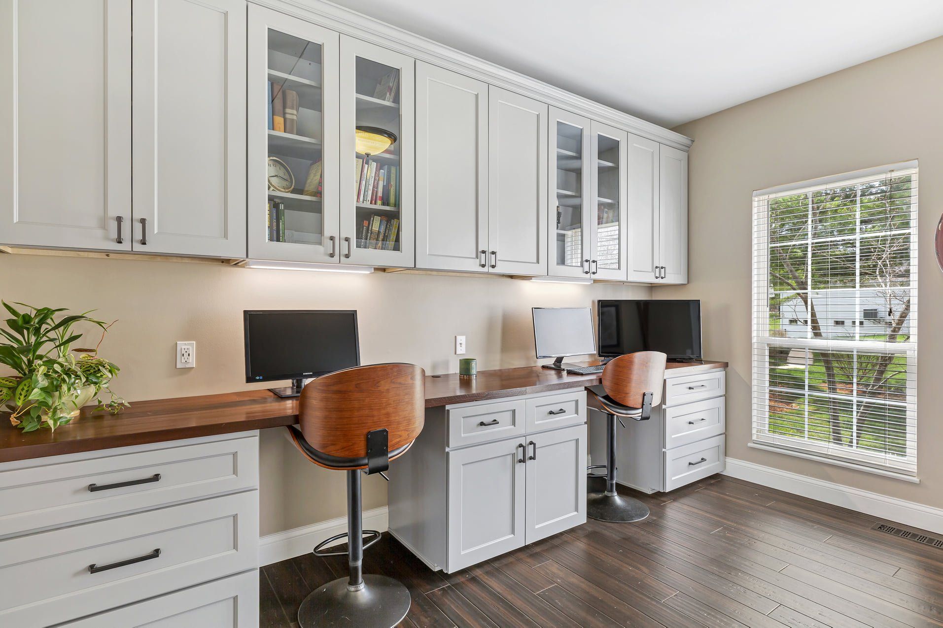 Home office with white cabinets, two desks, black chairs, and a large window.