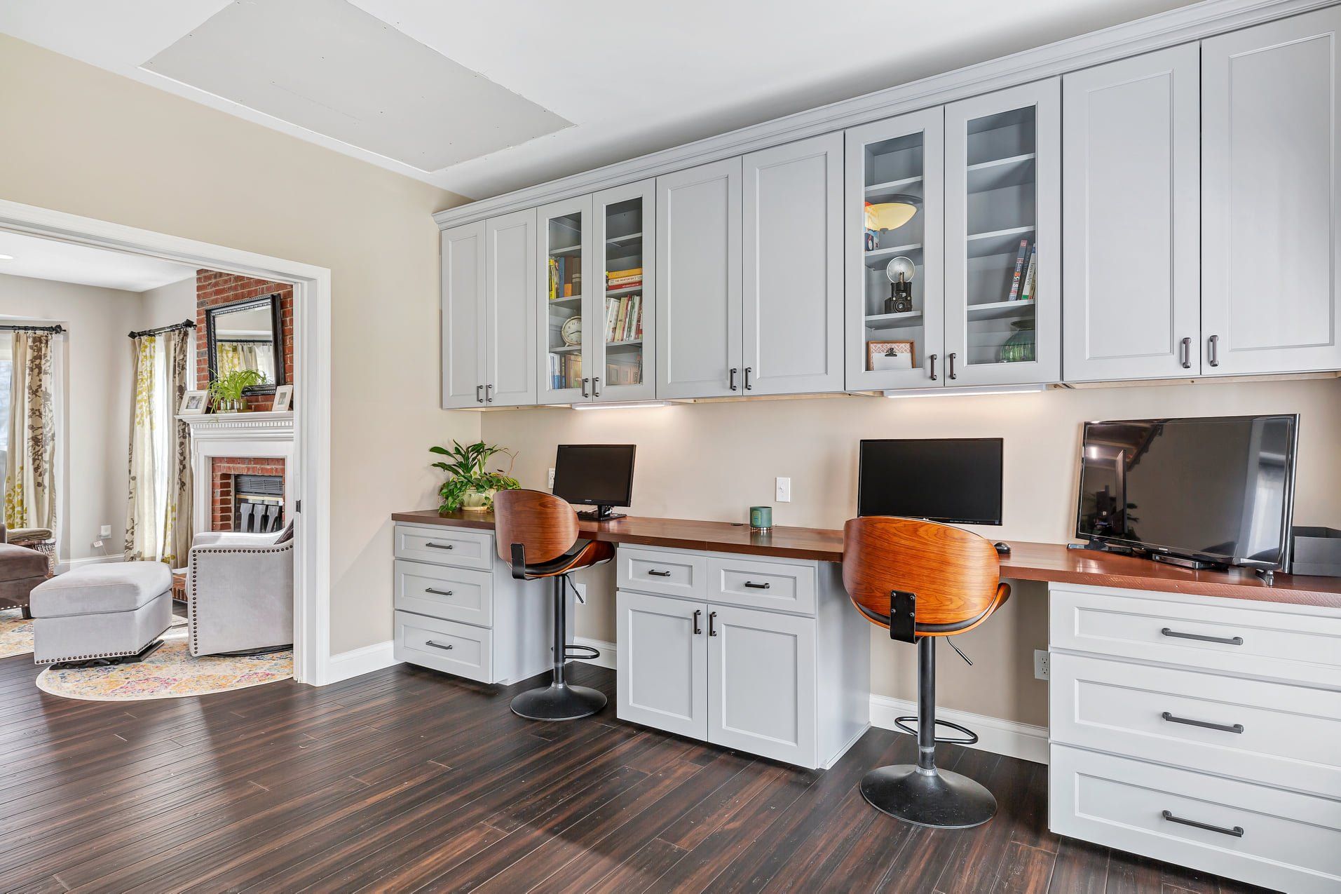 Bright home office with gray cabinets, white desks, orange chairs, and dark wood floors