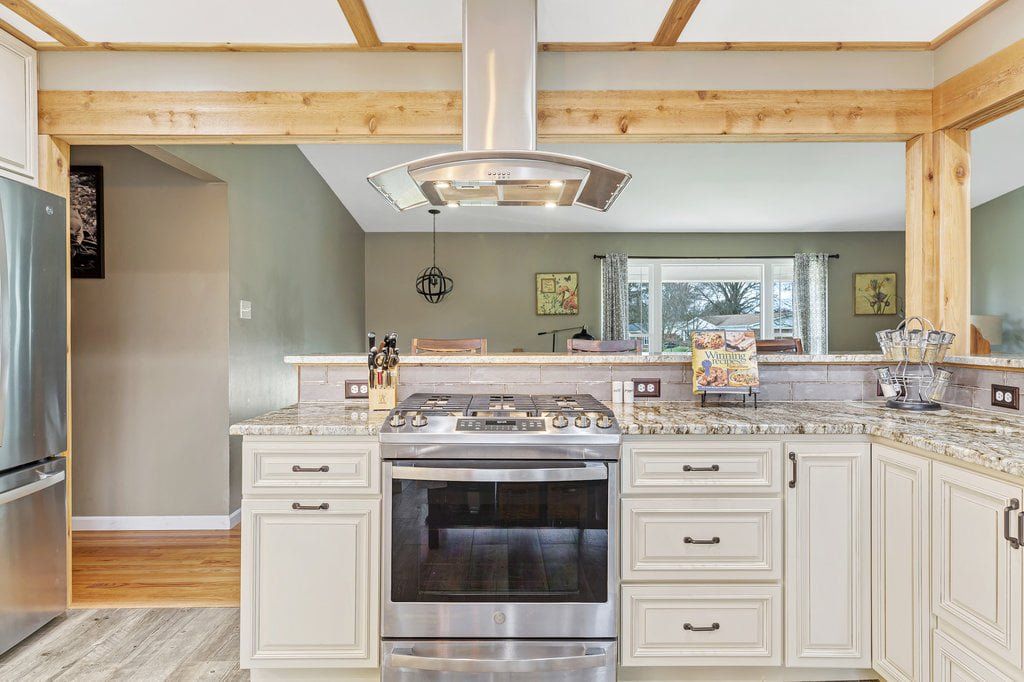 Bright kitchen with white cabinets, stainless steel stove, and wood beams over a central island