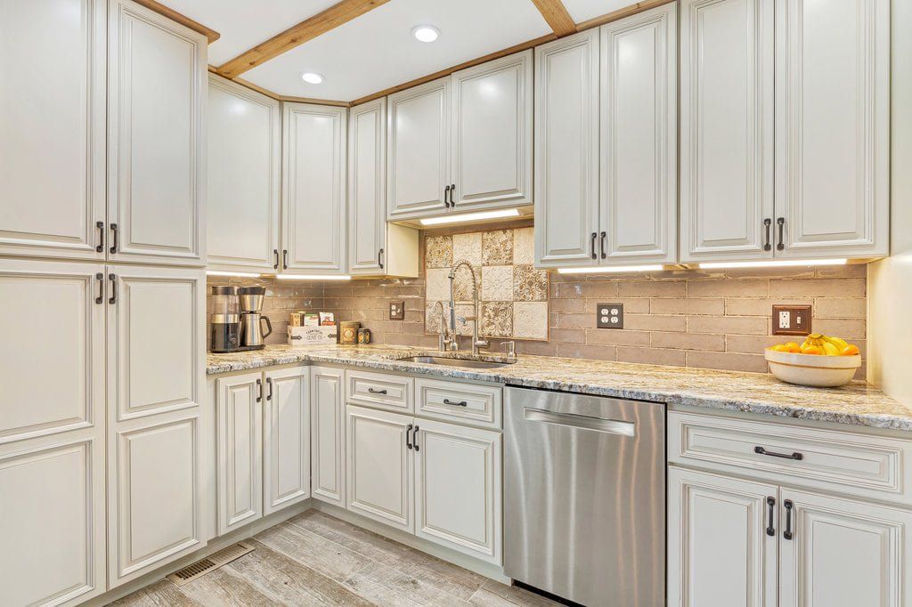Bright white kitchen with shaker cabinets, stainless dishwasher, beige countertops, and under-cabinet lighting.