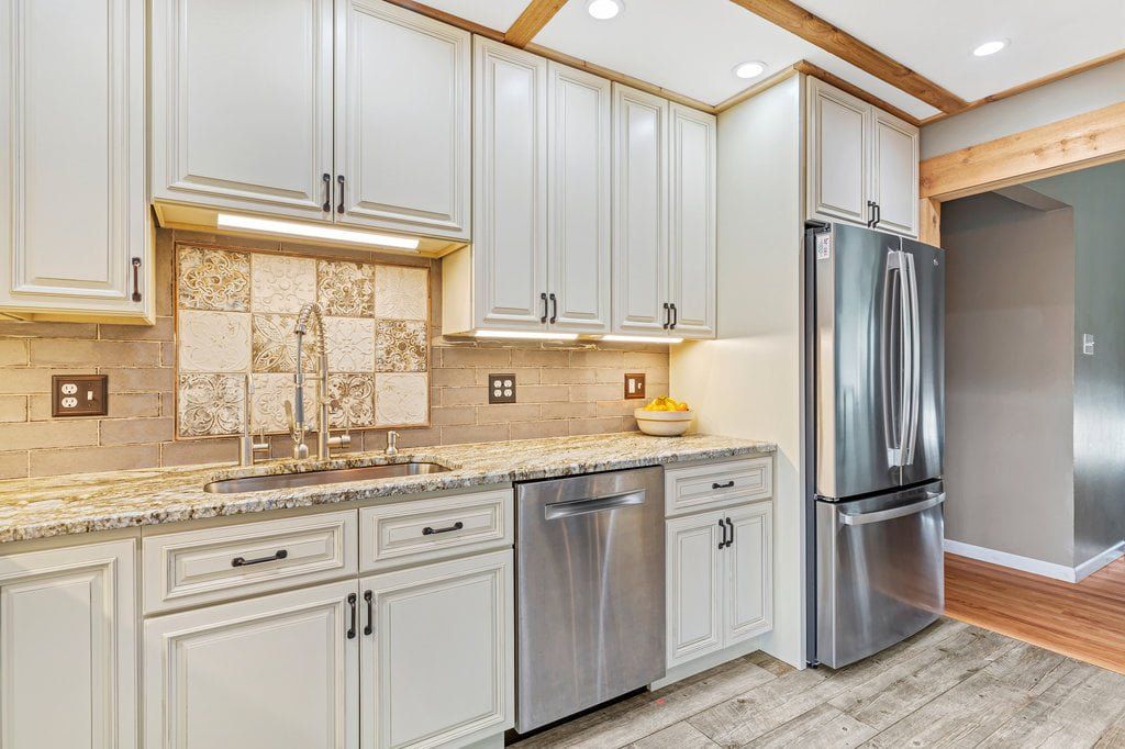 Bright modern kitchen with white cabinets, granite counters, stainless dishwasher and refrigerator, and tile backsplash