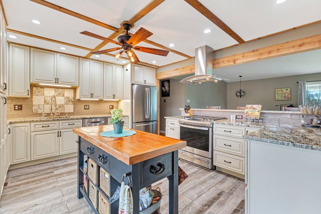 Bright modern kitchen with white cabinets, stainless appliances, wood island, and ceiling fan