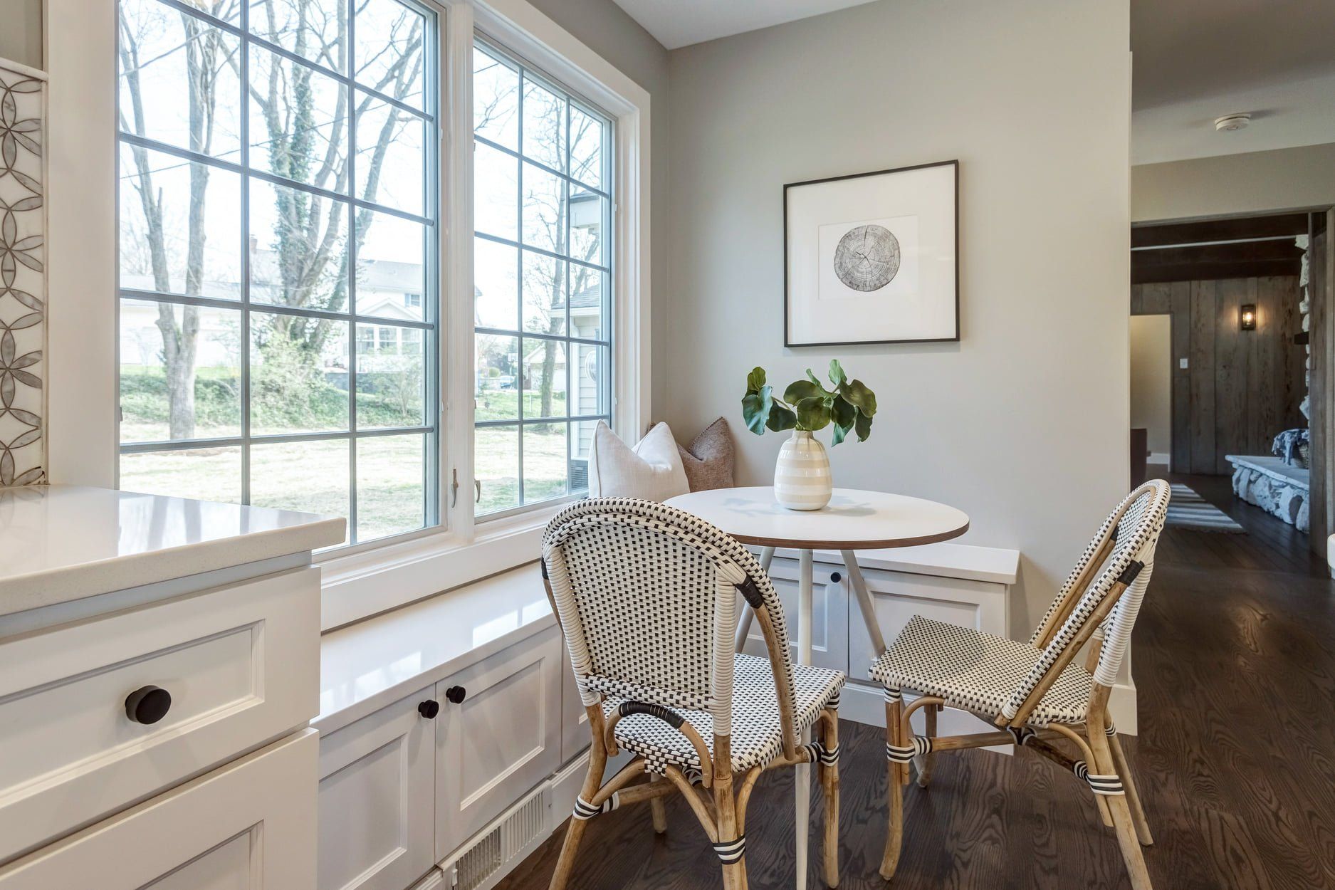 Bright breakfast nook with round table, woven chairs, and large windows overlooking trees