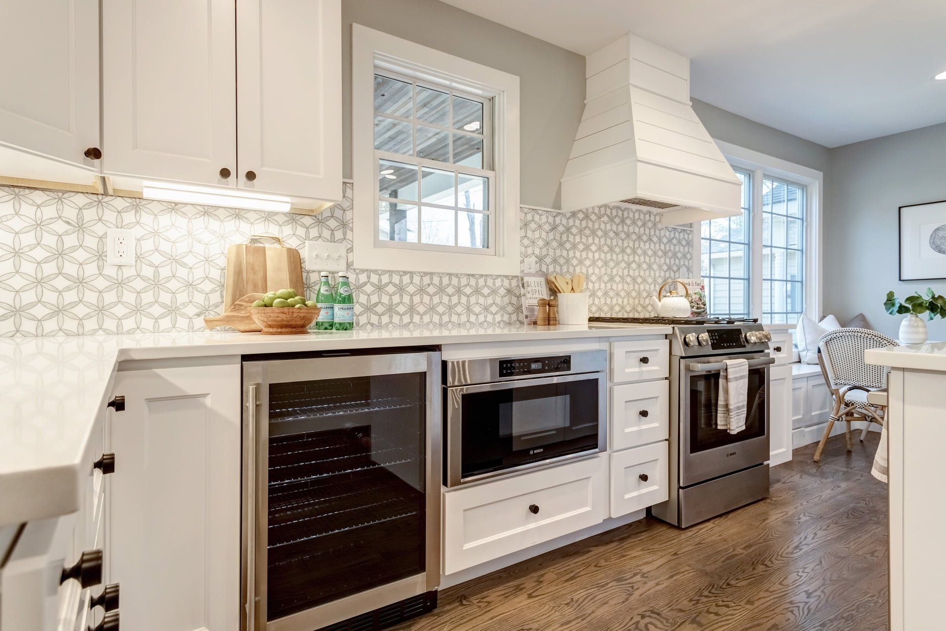 Bright white kitchen with stainless appliances, patterned backsplash, and wood floor leading to a dining area