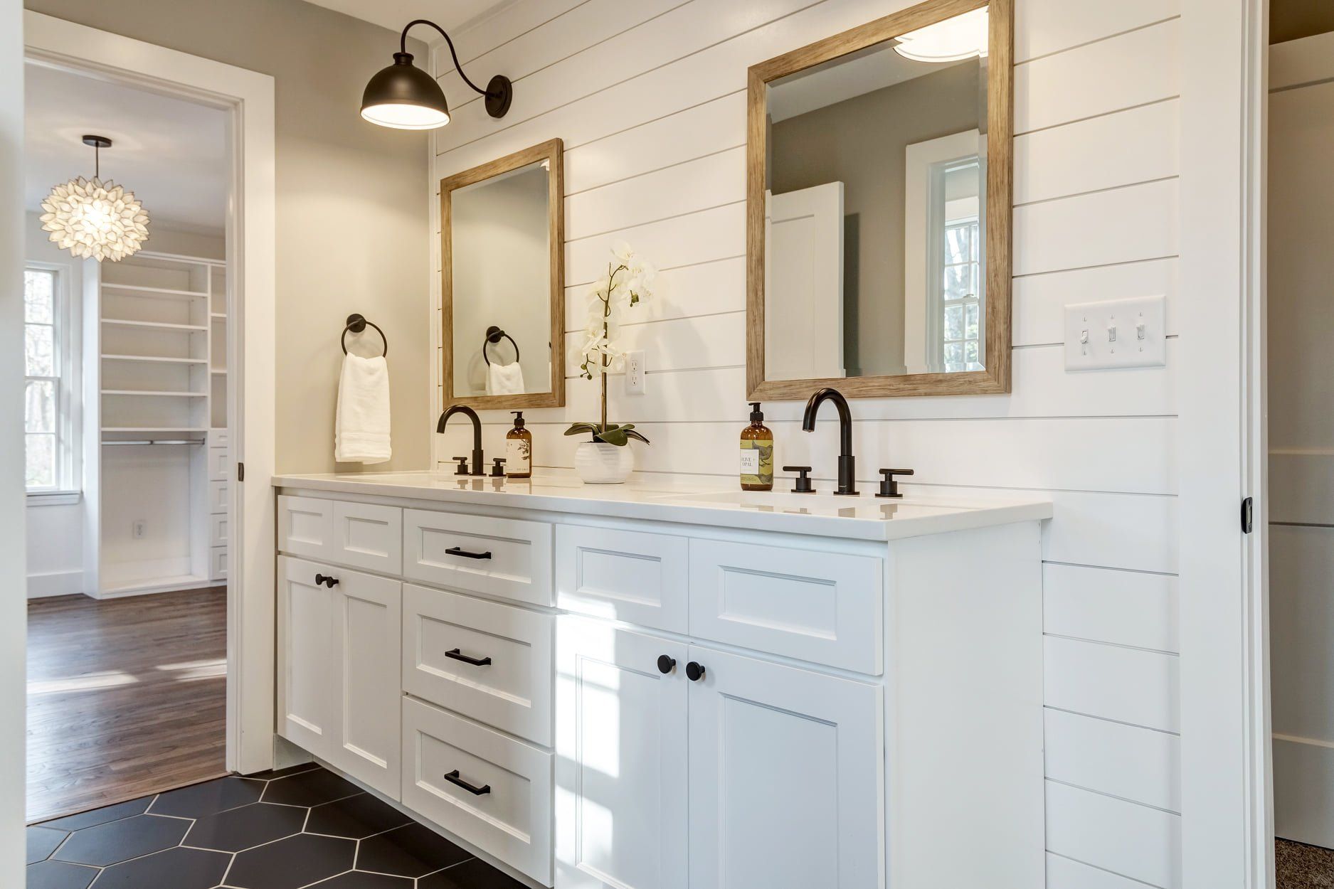 Bright white bathroom vanity with double sinks, gold mirrors, black fixtures, and shiplap walls