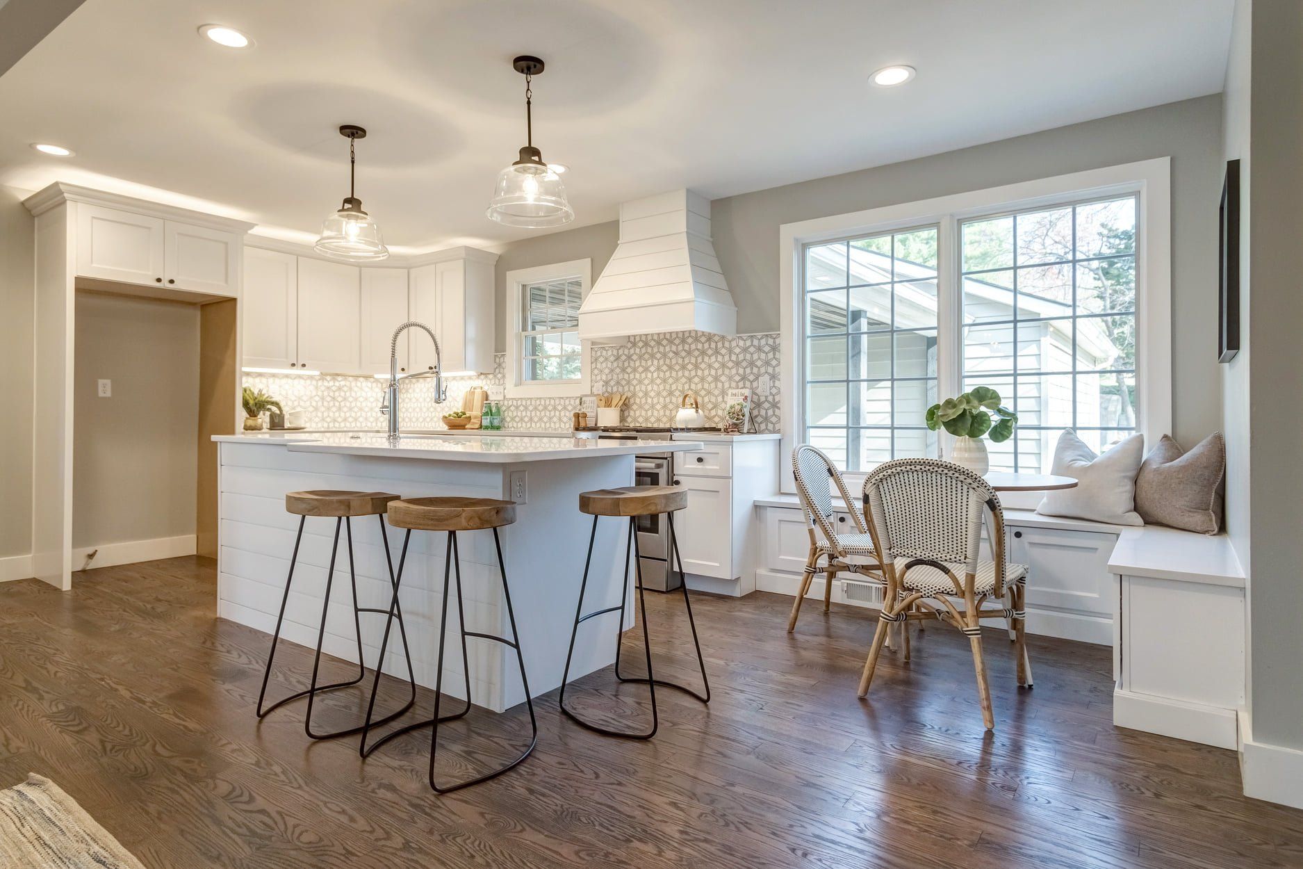 Bright kitchen with white cabinets, island stools, pendant lights, and a cozy window bench seat