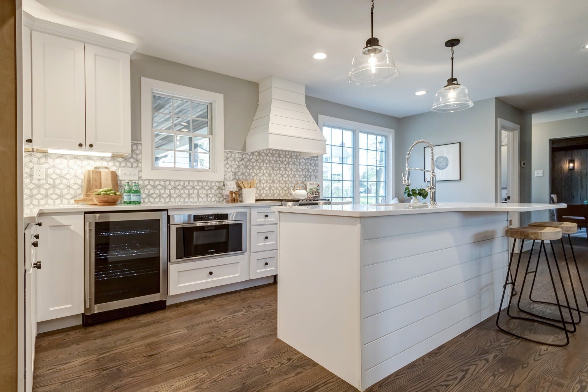Bright modern kitchen with white cabinets, island, stainless appliances, and wood floors