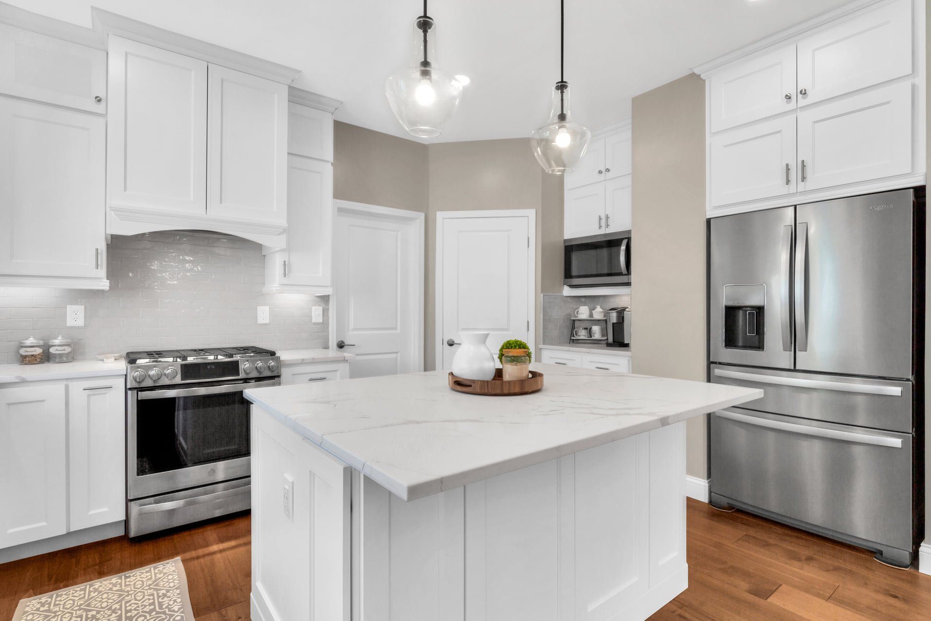 Bright white modern kitchen with stainless steel appliances and central island, lit by pendant lights