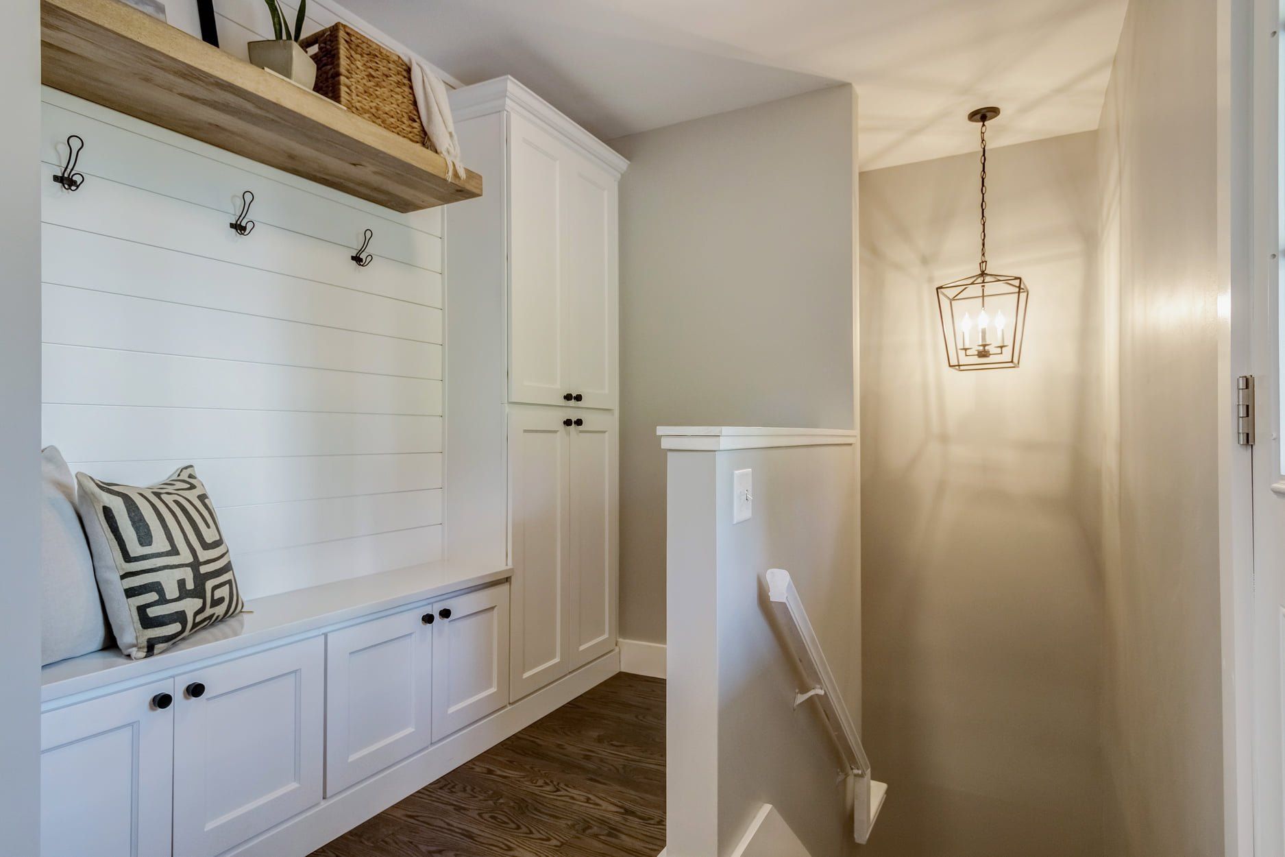 Bright hallway with built-in bench, hooks, white cabinets, and a hanging lantern light