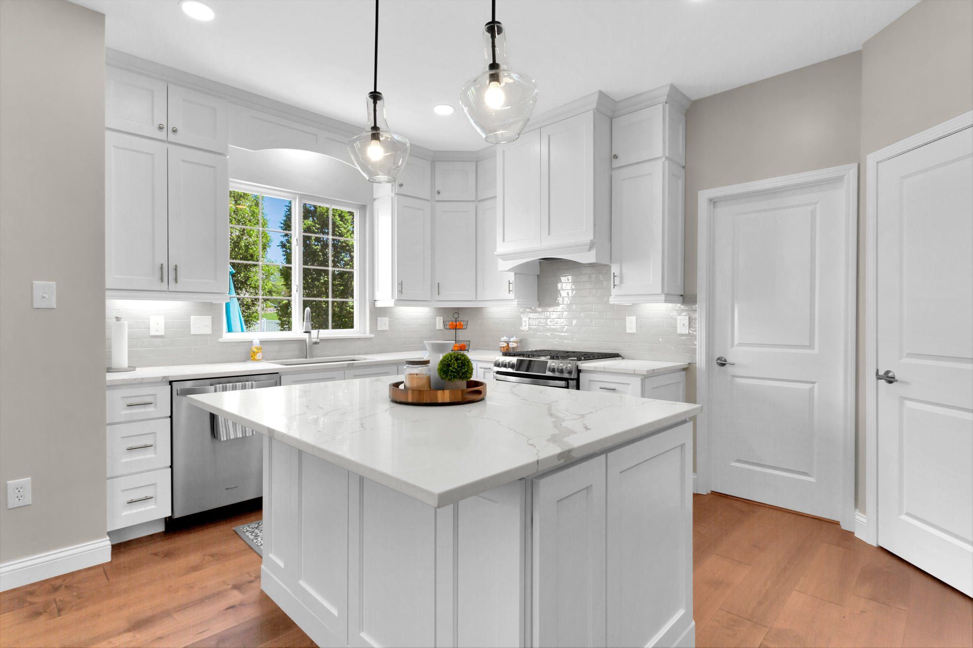 Bright white kitchen with island, gray cabinets, pendant lights, and hardwood floors