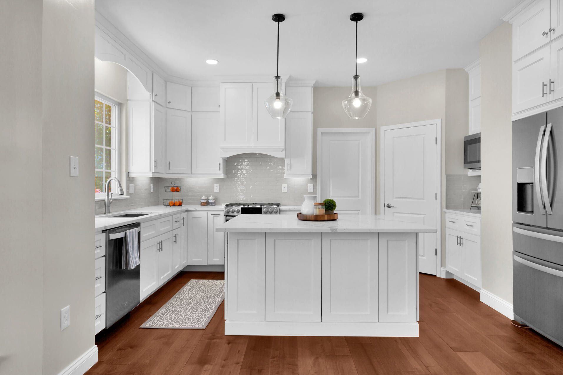 Bright white modern kitchen with island, pendant lights, stainless appliances, and hardwood floors