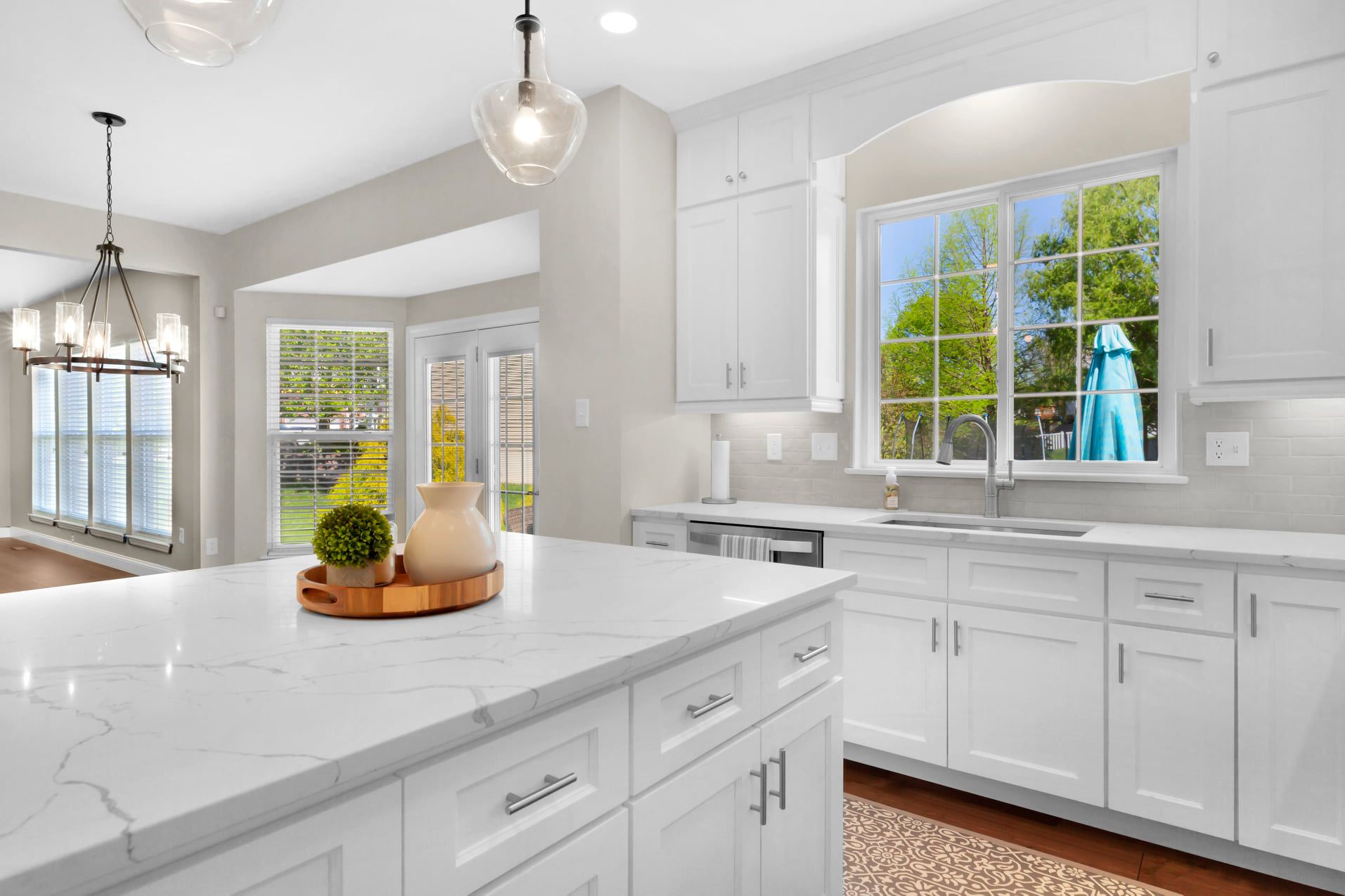 Bright white kitchen with marble island, pendant lights, and large window over sink