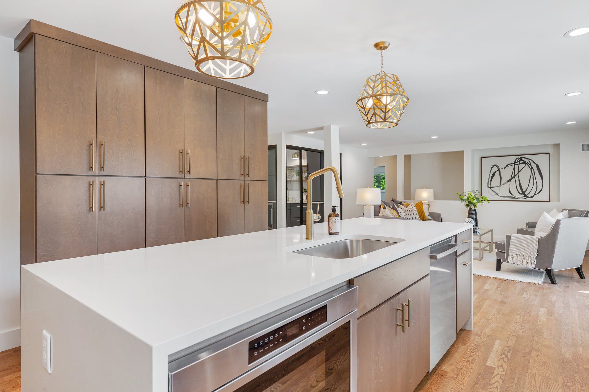 Modern open kitchen with white island, wood cabinets, gold pendant lights, and bright dining area