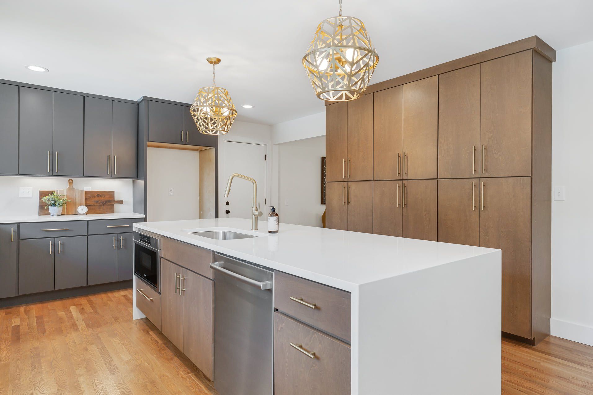 Modern kitchen with dark cabinets, large white island, wood floors, and two pendant lights