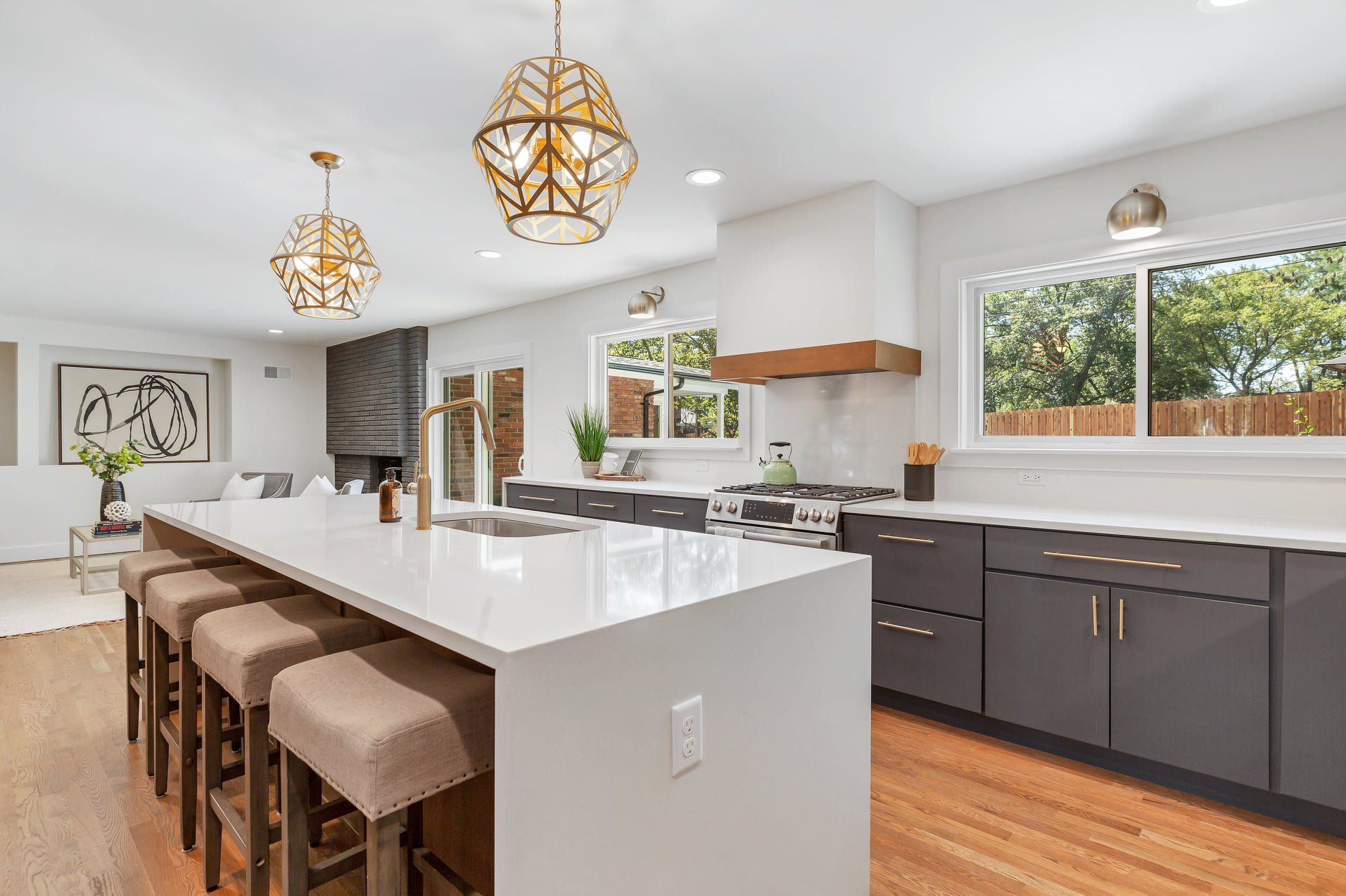 Bright modern kitchen with white island, brown stools, dark cabinets, and gold pendant lights