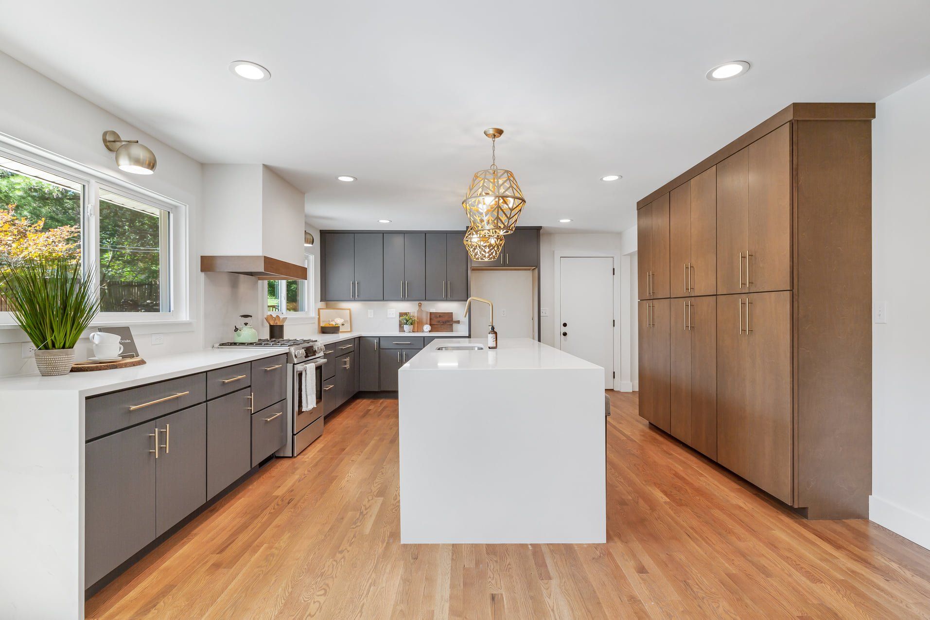 Modern kitchen with white island, gray cabinets, wood floors, and large wooden pantry cabinets