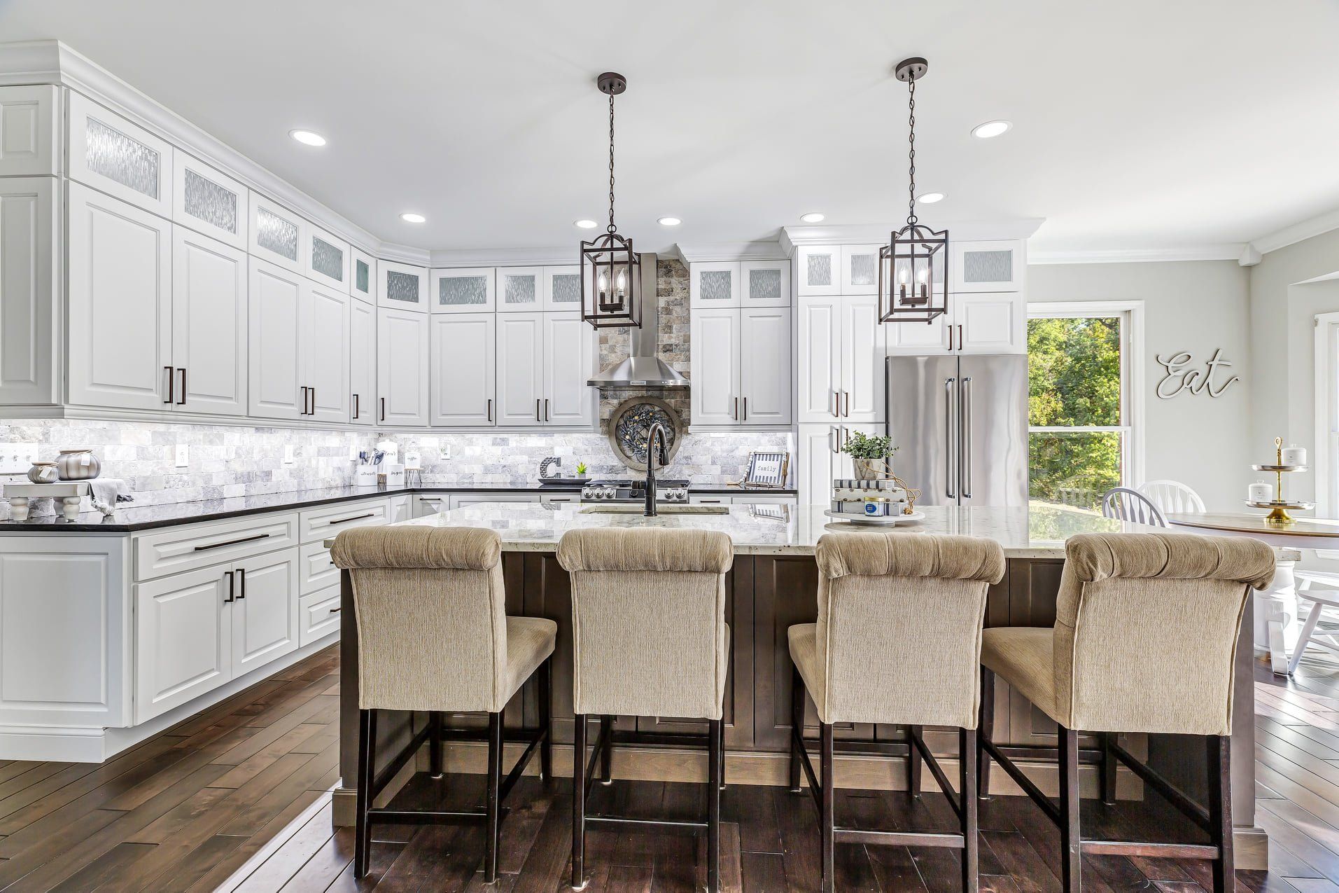 Bright white kitchen with large island, barstools, pendant lights, and dark wood floors