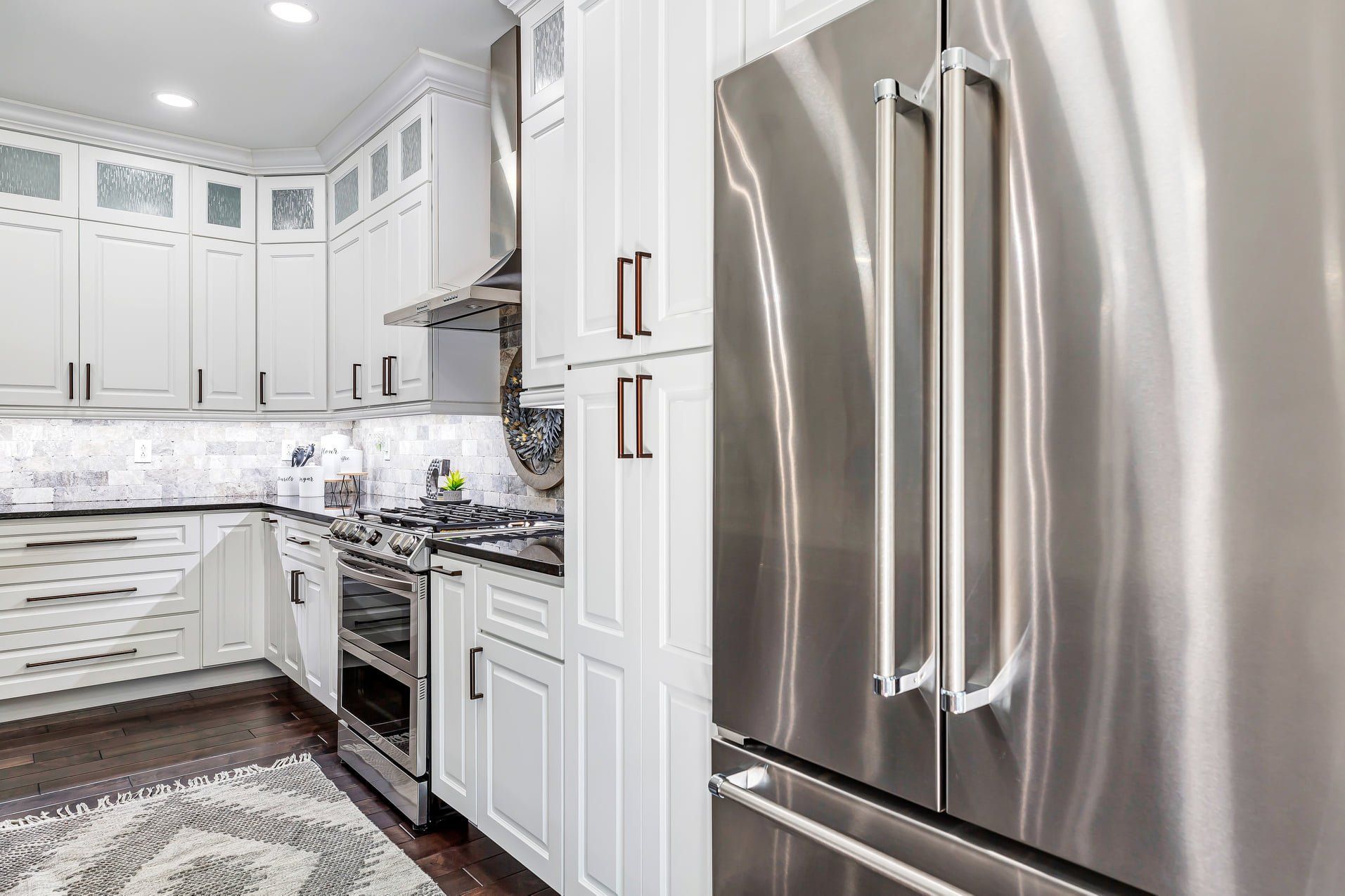 Bright white kitchen with stainless steel refrigerator, stove, and cabinets under recessed lighting