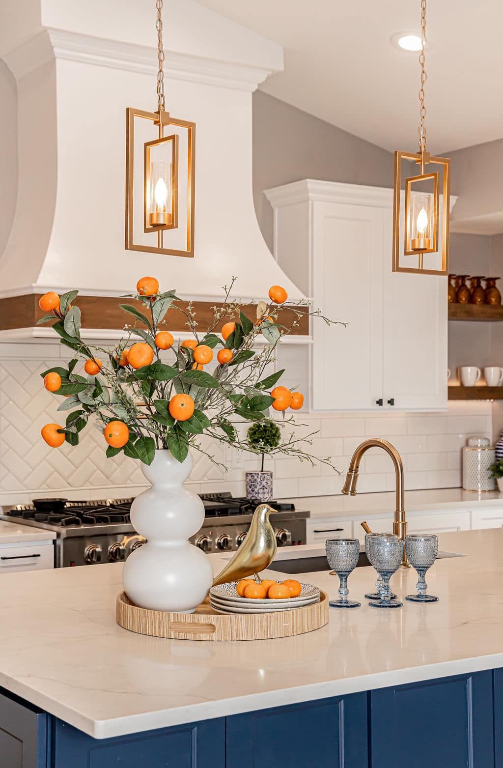 Stylish kitchen island with white flowers, oranges, blue cabinetry, and hanging pendant lights