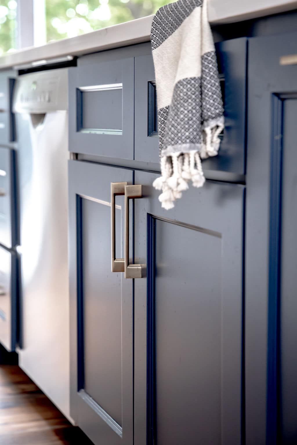 Dark blue kitchen cabinets with a hanging gray-and-white towel by a sunlit countertop