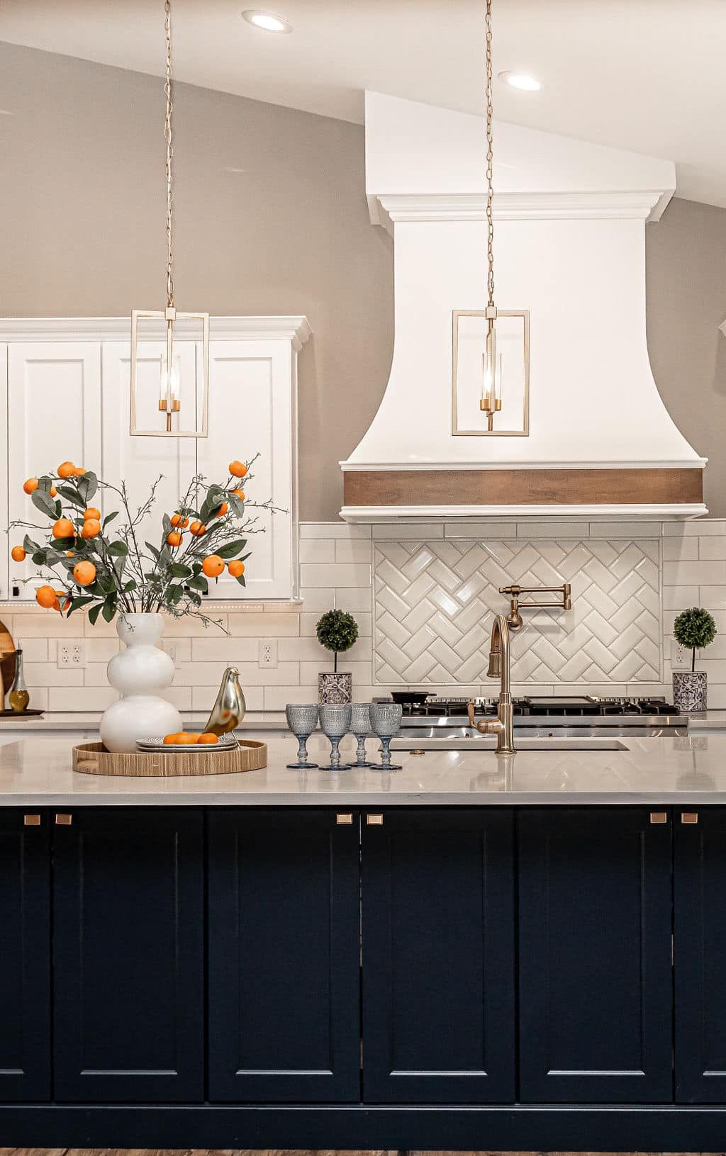 Elegant kitchen with navy cabinets, white backsplash, brass pendants, and a vase of flowers on the counter