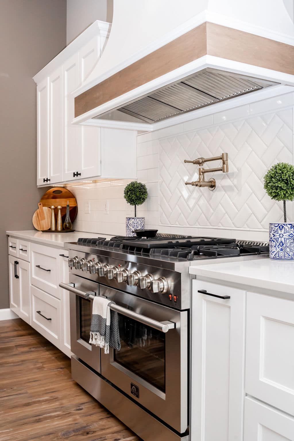 Bright white kitchen with stainless stove, marble countertops, and wood flooring under a vent hood