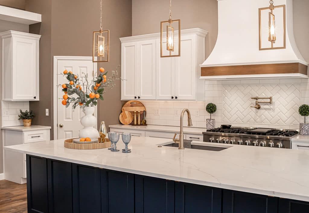Modern white kitchen with navy island, brass pendant lights, and a marble countertop with flowers and decor