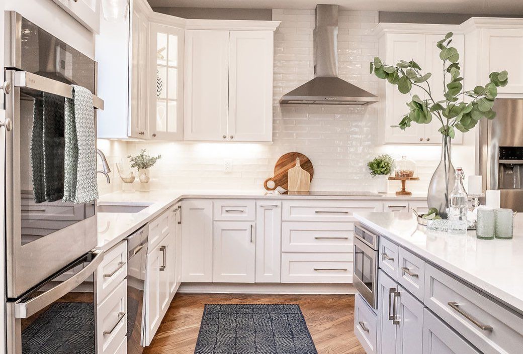 Bright white kitchen with stainless steel oven, island, and potted greenery under natural light