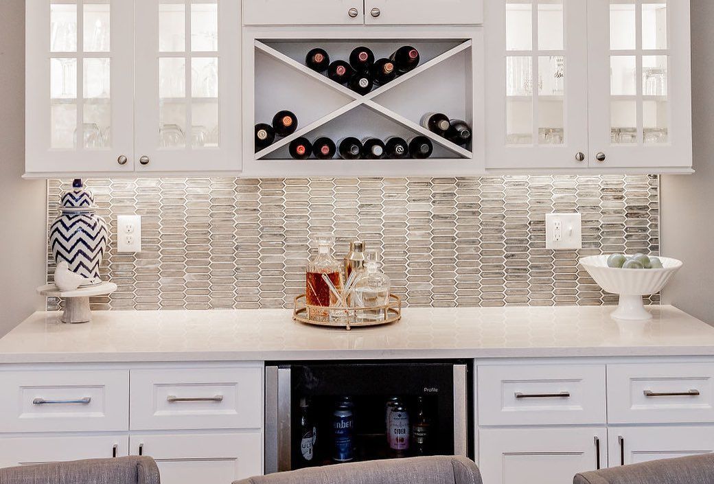 Bright white kitchen bar with mosaic backsplash, wine rack, cabinets, and decorative jars on the counter