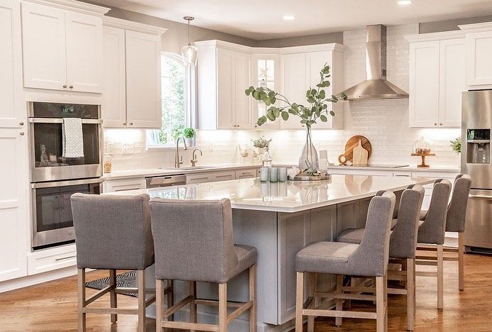 Bright modern kitchen with white cabinets, island, and gray upholstered chairs