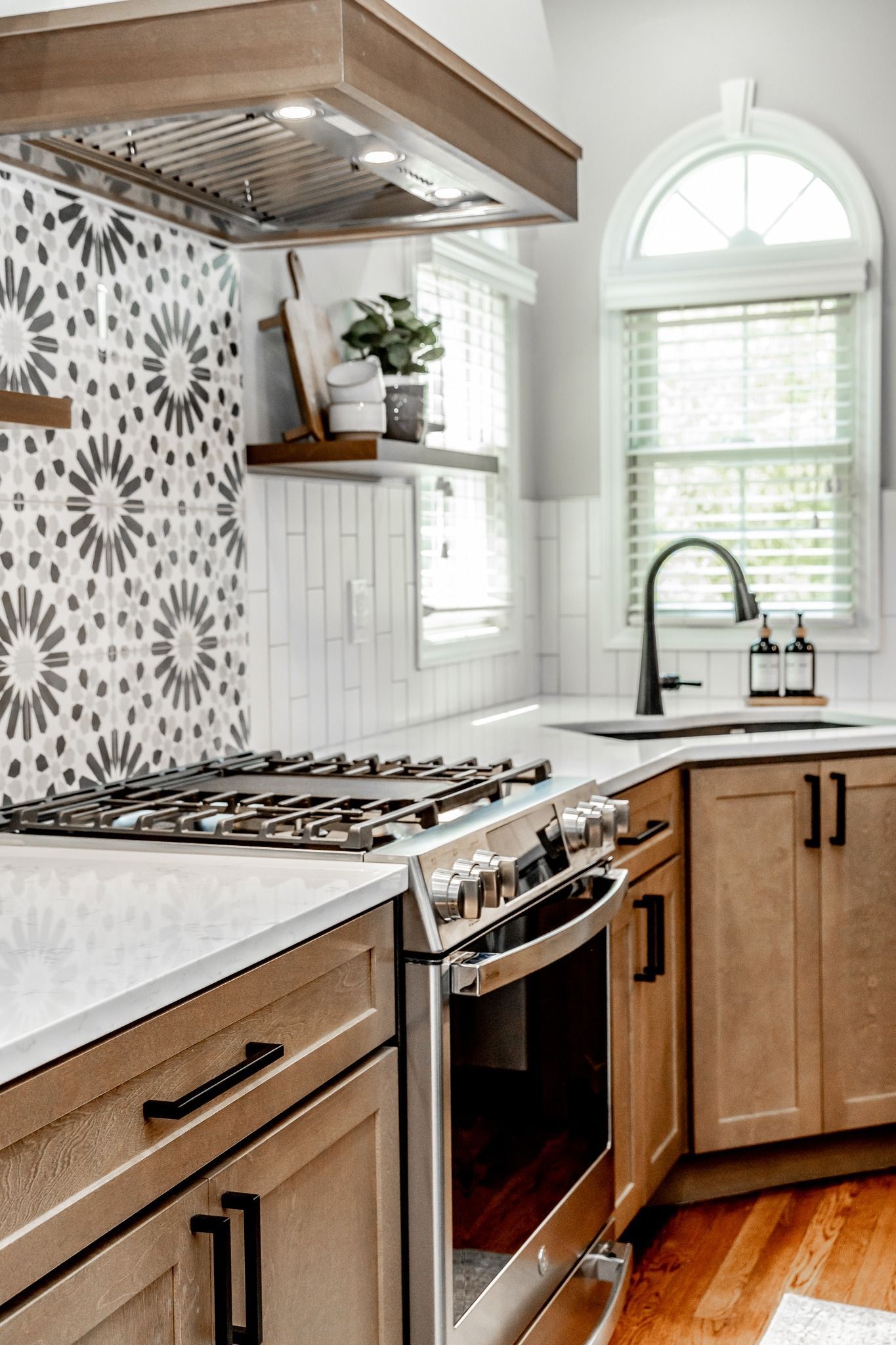 Bright modern kitchen with wood cabinets, patterned tile backsplash, stove, sink, and arched window.
