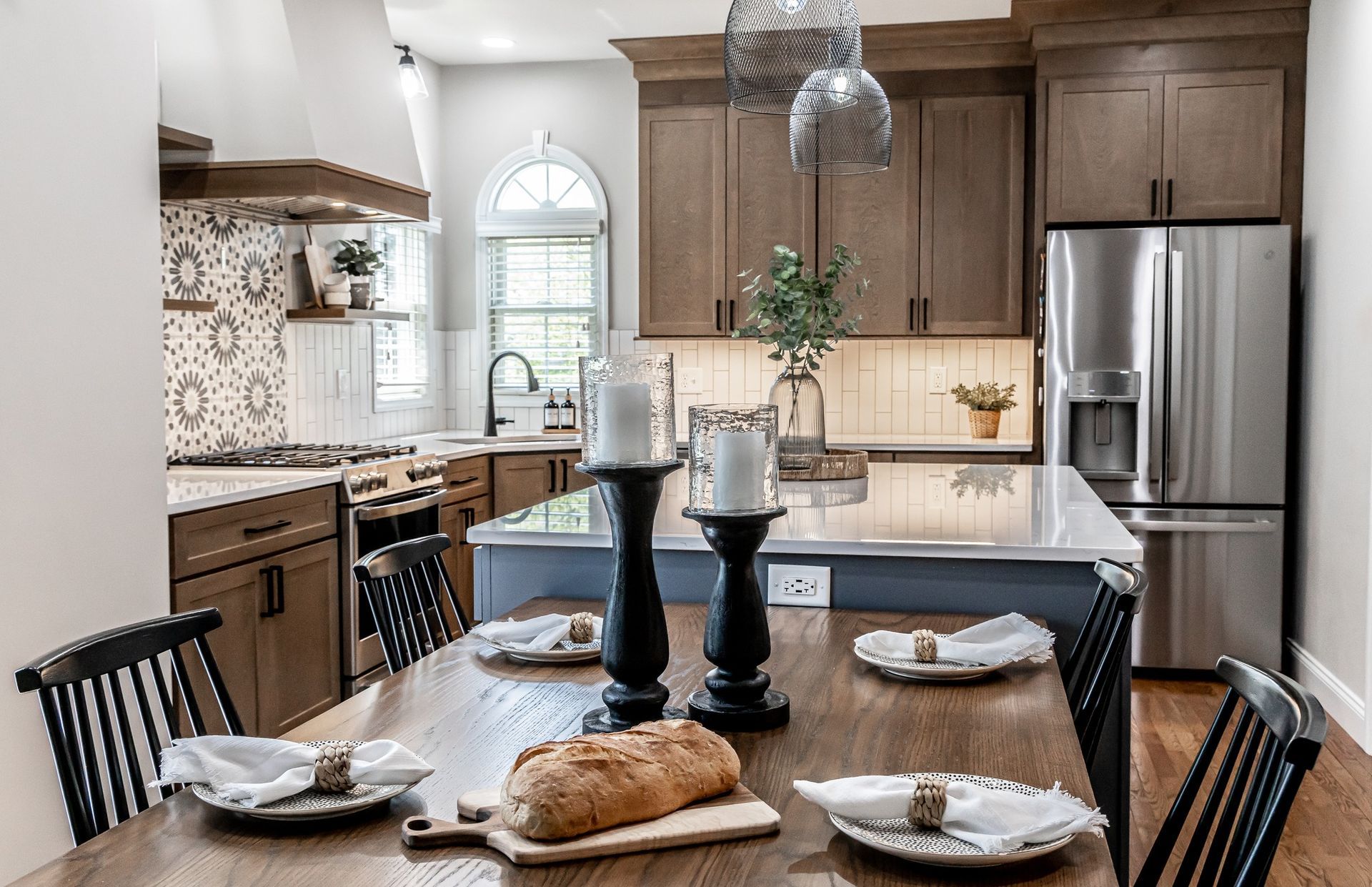 Modern kitchen with wood cabinets, stainless fridge, and a dining table set with bread and candles.