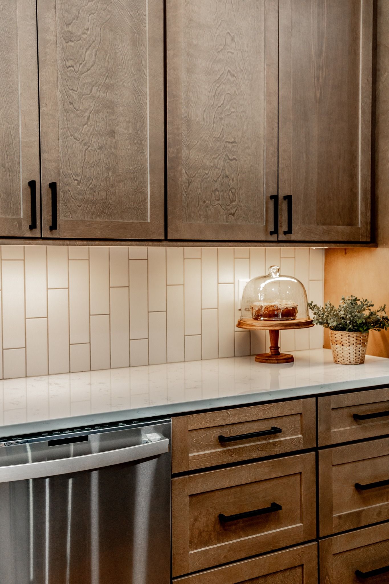 Modern kitchen with wood cabinets, white tile backsplash, marble countertop, and cake stand with pastries