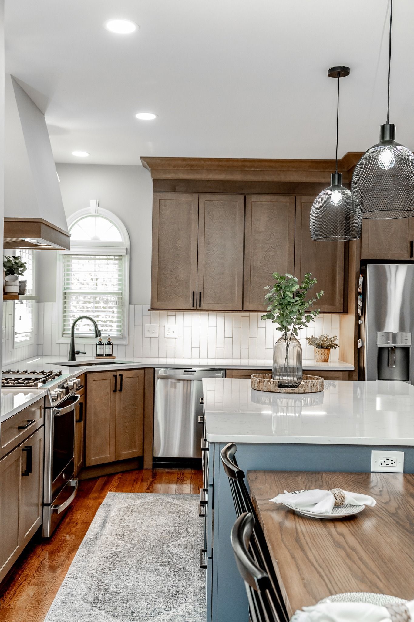 Bright kitchen with wood cabinets, stainless appliances, white island, and hanging pendant lights.