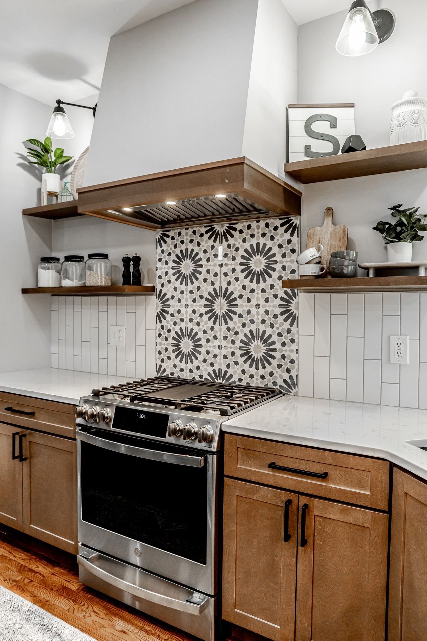 Modern kitchen with stainless steel stove, patterned tile backsplash, wood cabinets, and open shelves