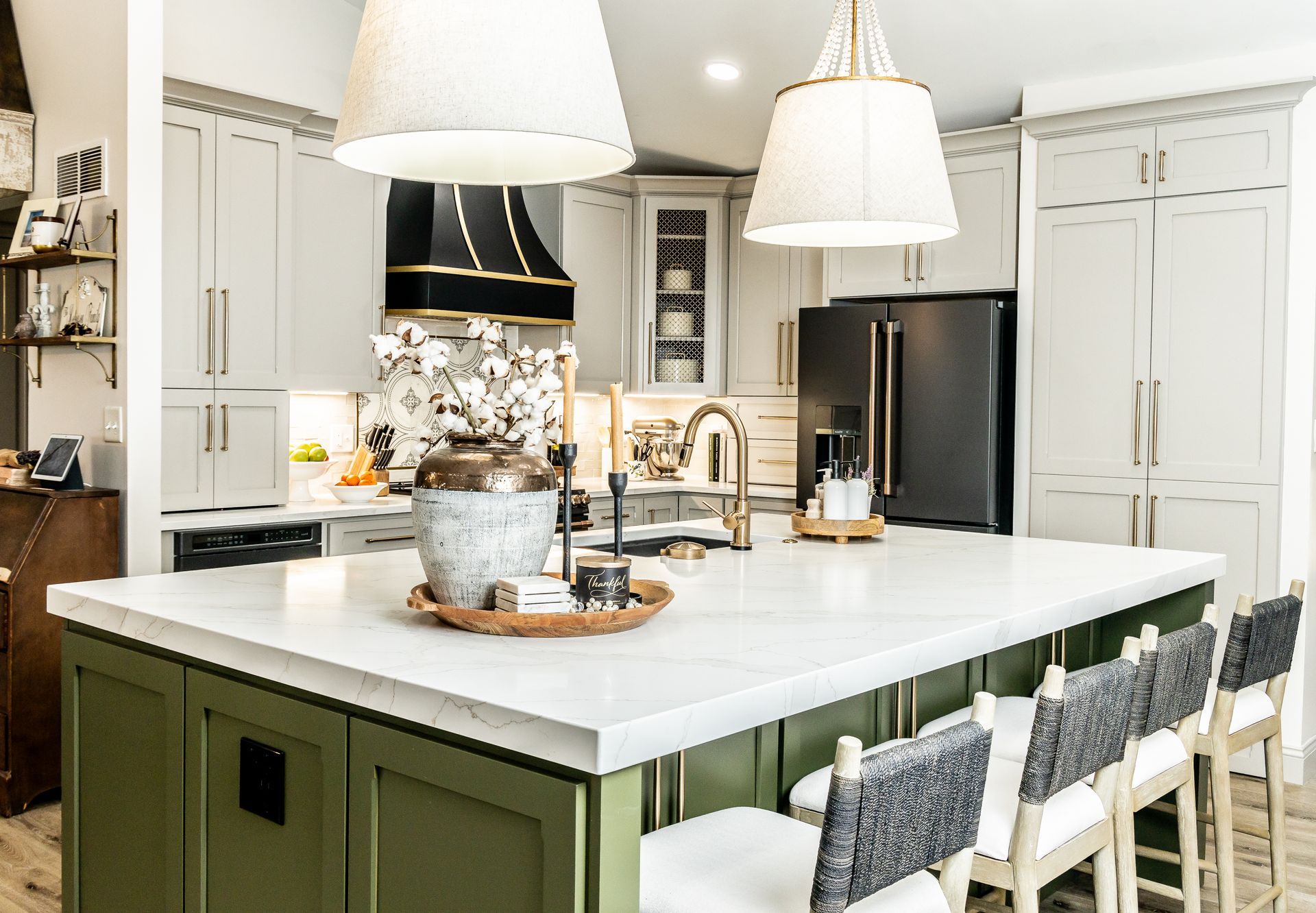 Modern white kitchen with a green island, pendant lights, and gray counter stools