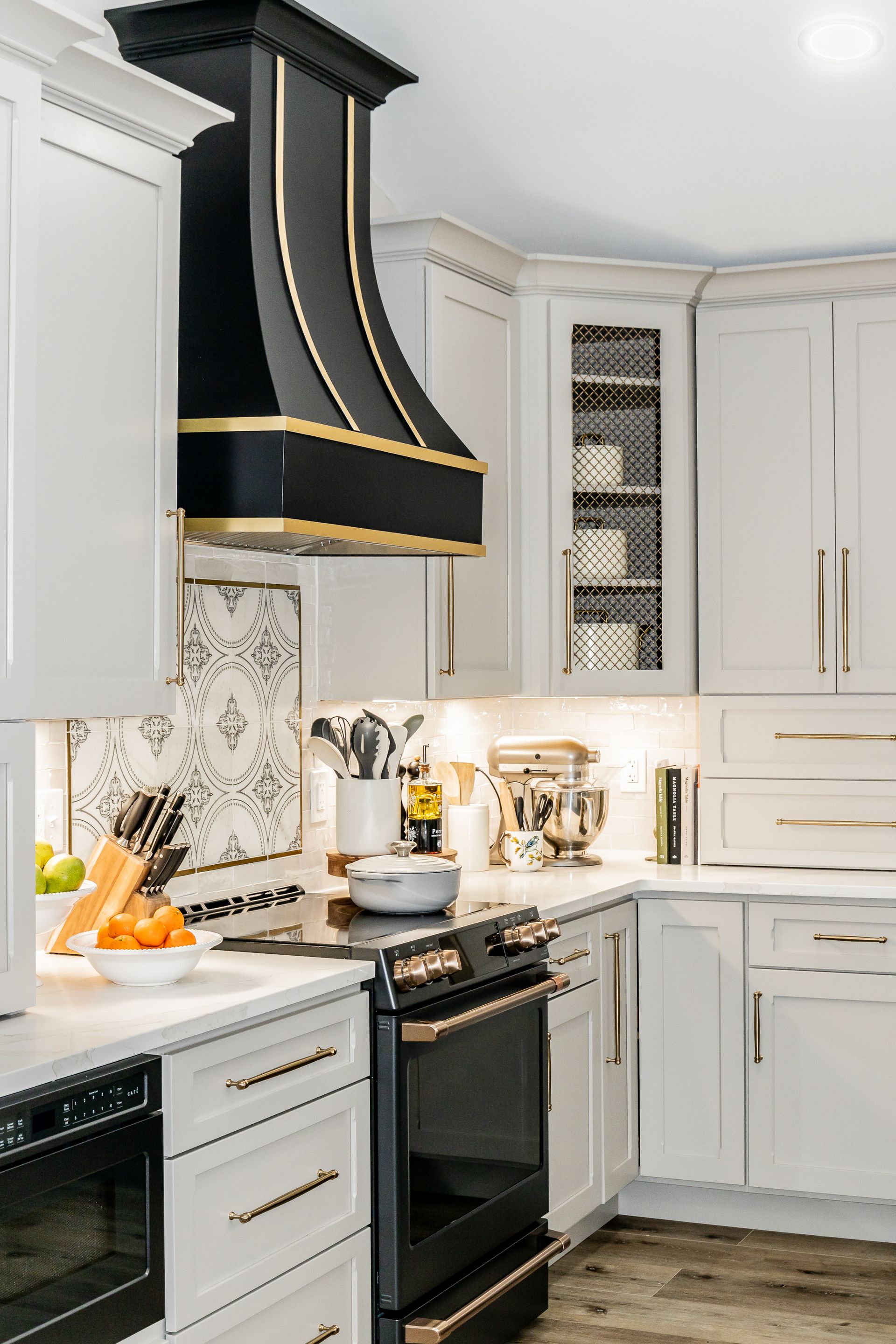 Bright white kitchen with gray cabinets, black range hood, and gold accents