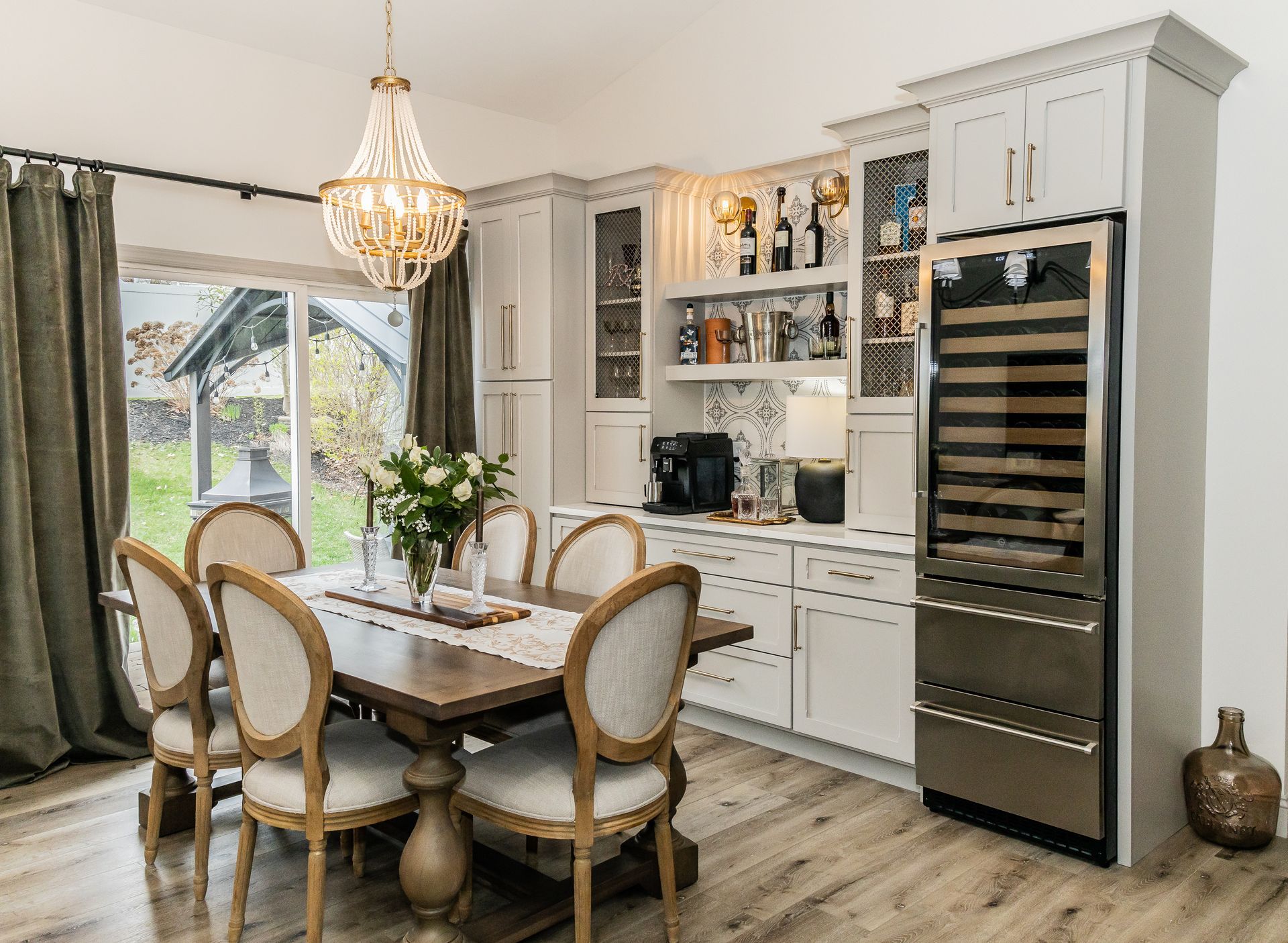 Elegant kitchen-dining area with white cabinets, gold chandelier, wood table, and wine cooler