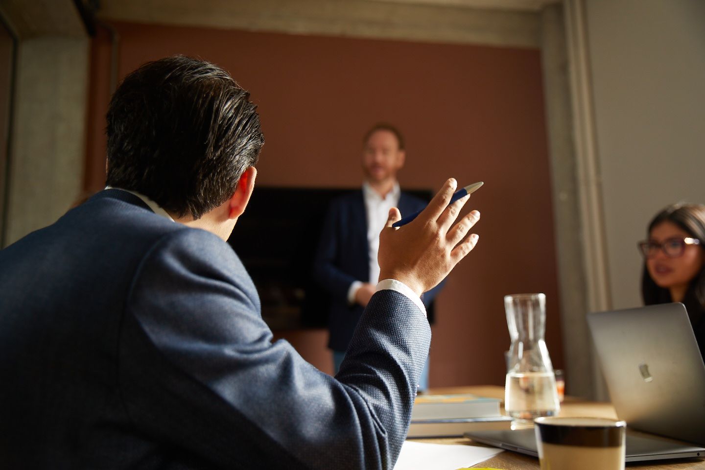 Een man in pak zit aan een tafel en praat met een andere man, als voorbeeld van een roleplay-oefening gericht op het toepassen van overtuigingstechnieken.