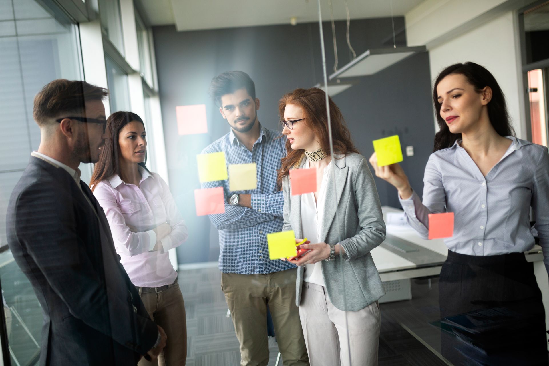 Een groep mensen staat rond een glazen wand met daarop post-its.