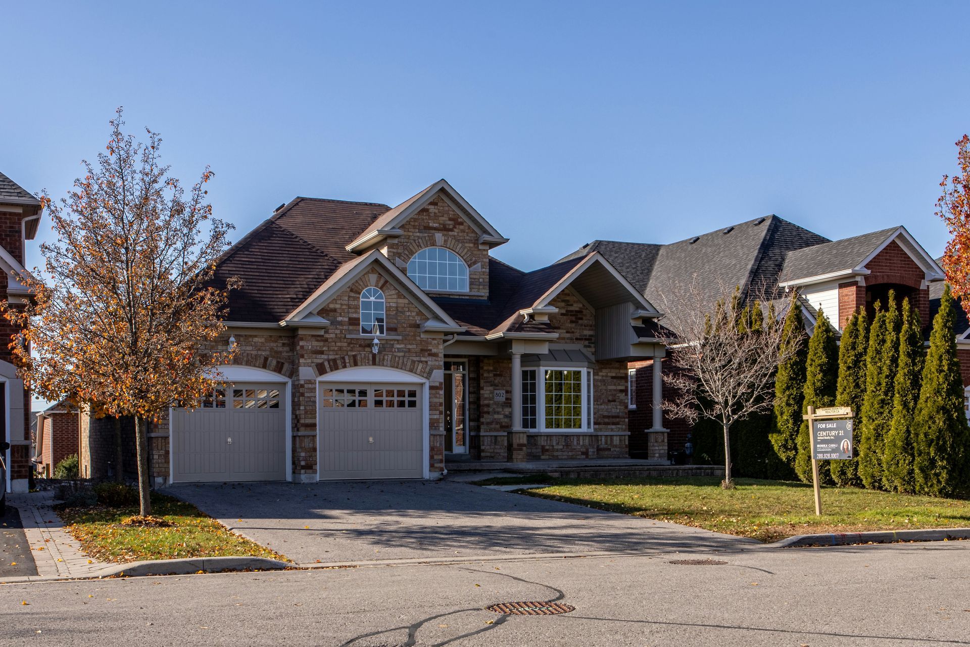 Drone Suburban brick house with three-car garage and autumn trees on a quiet street