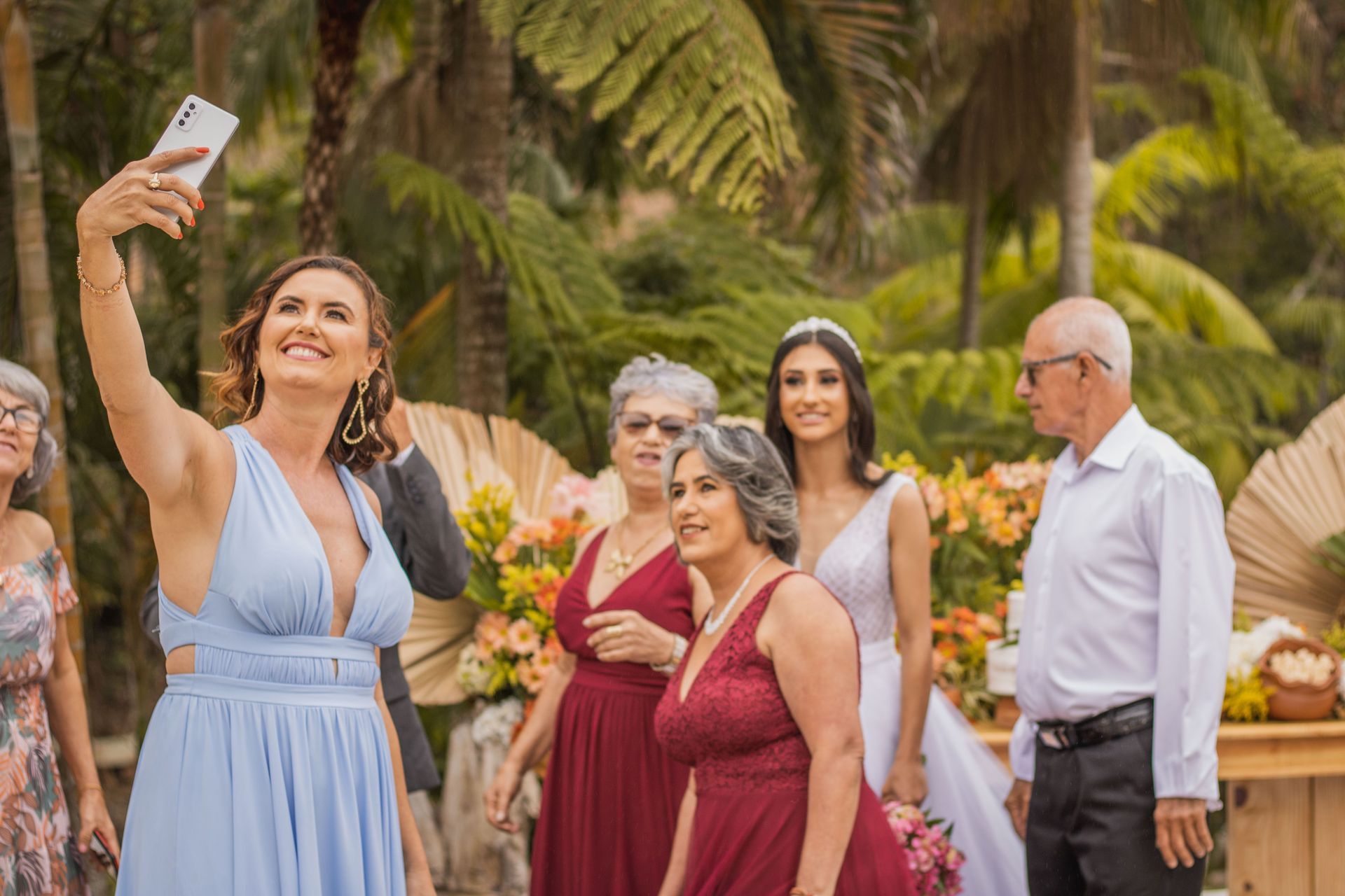 Drone Group of people posing outdoors as one woman in a light blue dress takes a selfie in a garden.