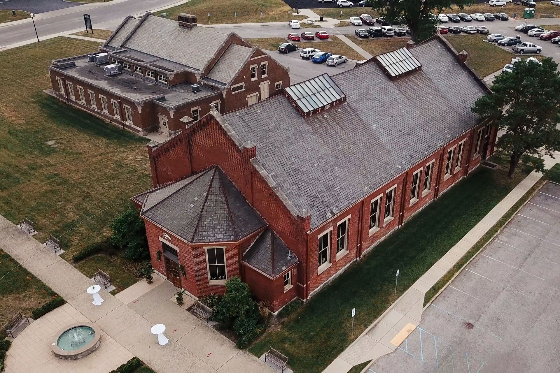 Drone Aerial view of a red-brick building with a gray roof and small courtyard beside a street.