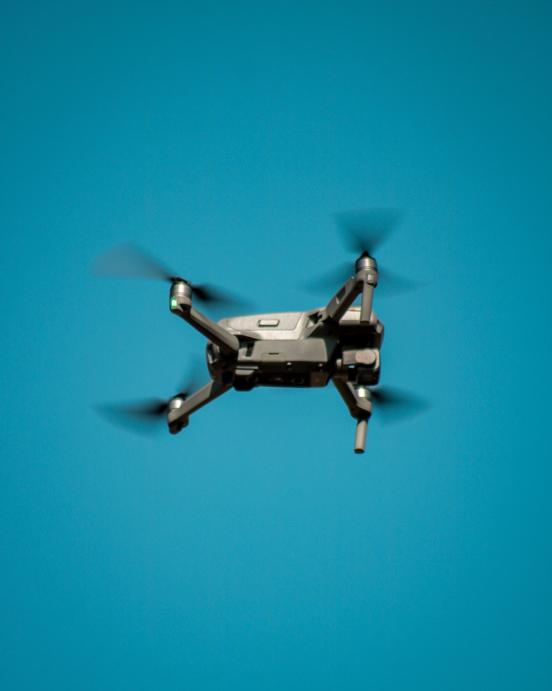 Drone Black drone with spinning propellers against a bright blue background.