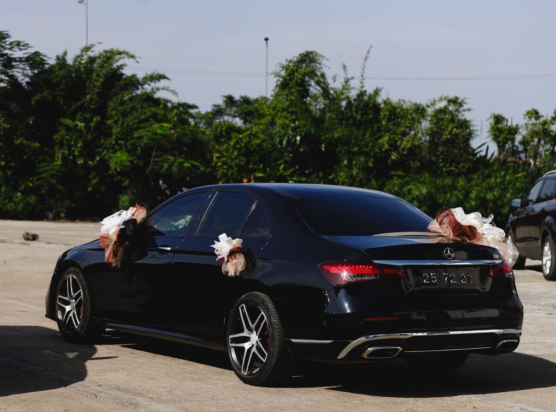 Drone Black sedan decorated with white bows parked on a sunny roadside with greenery in the background