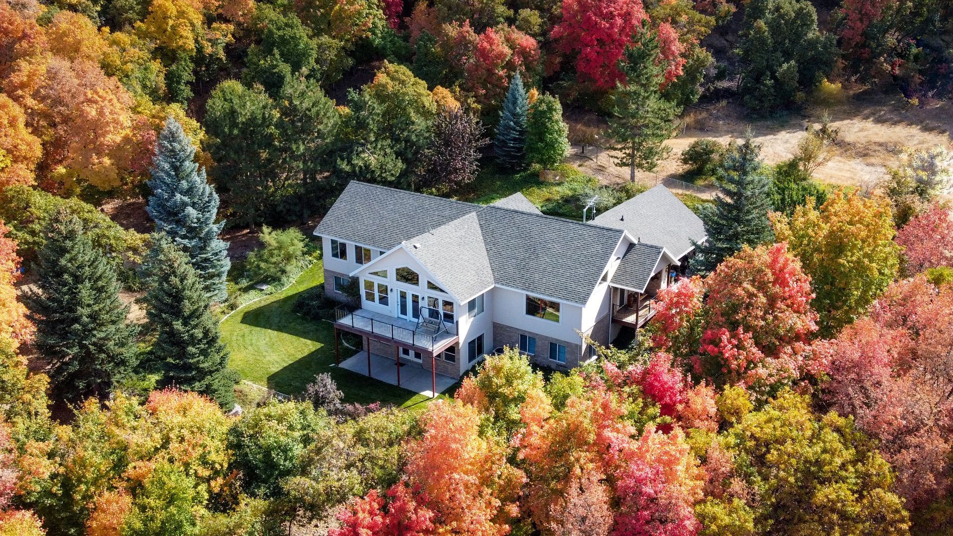 Drone Aerial view of a white house with a gray roof surrounded by colorful autumn trees