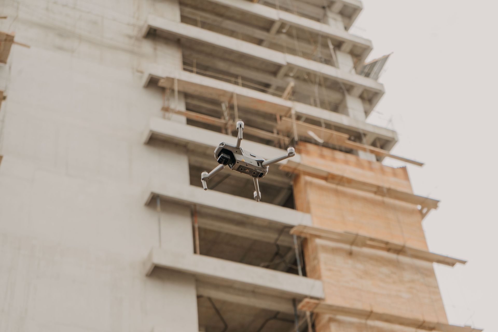 Drone flying beside a high-rise building under construction, with scaffolding and exposed floors.