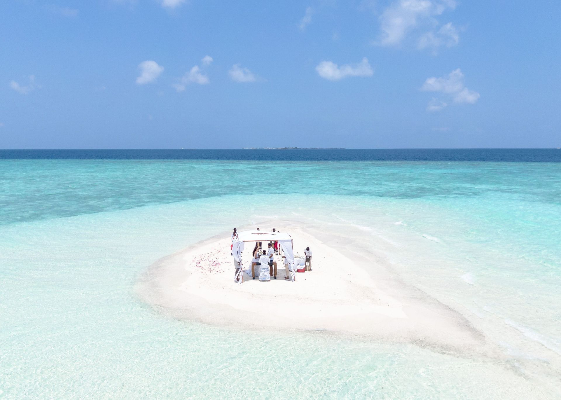 Drone Tiny group on a white sandbar in turquoise ocean under a bright blue sky.