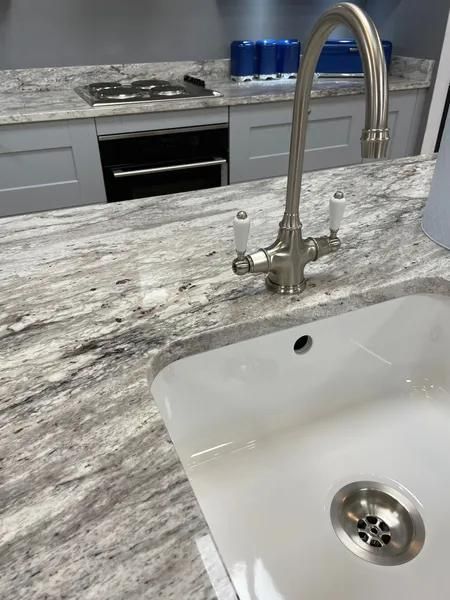 Kitchen sink with faucet on a stone countertop; oven and stovetop visible in the background.