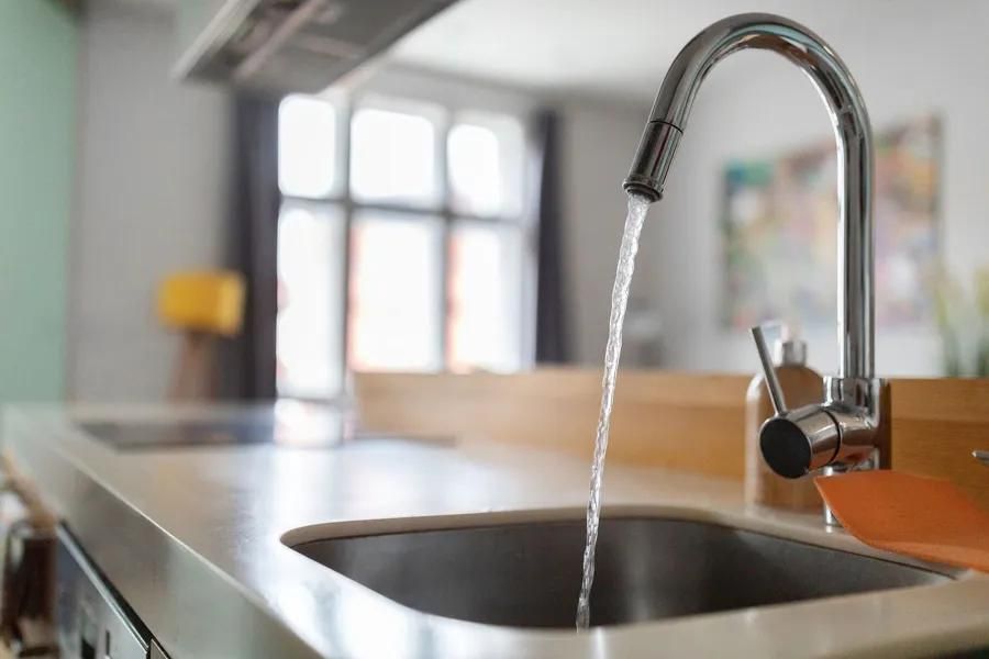 A kitchen faucet with water running into a stainless steel sink, near a countertop and window.